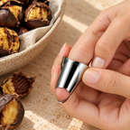 Close-up of a stainless steel finger guard fitted over a fingertip, with roasted chestnuts in the background
